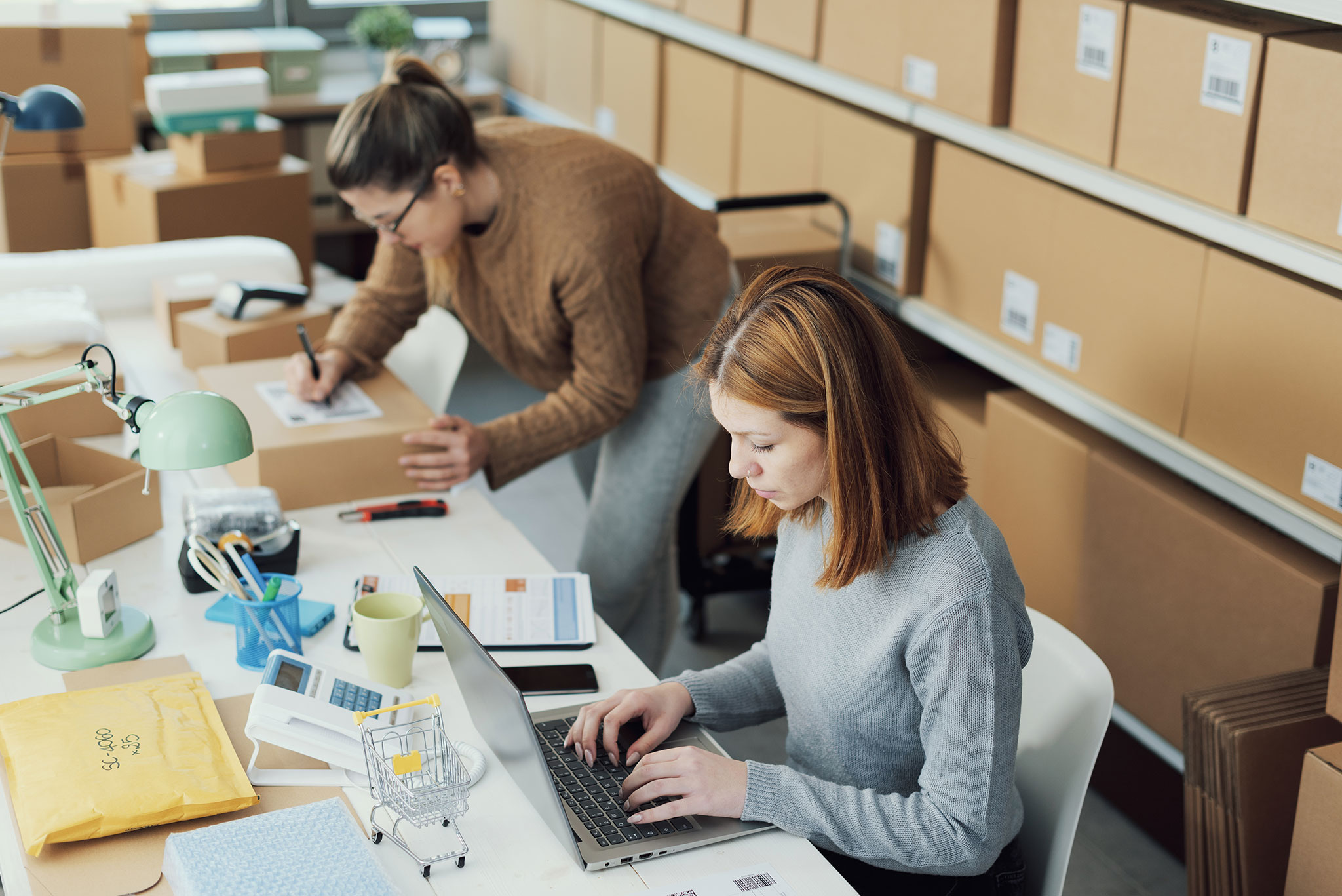 Women in warehouse working on computers near shelves of boxes